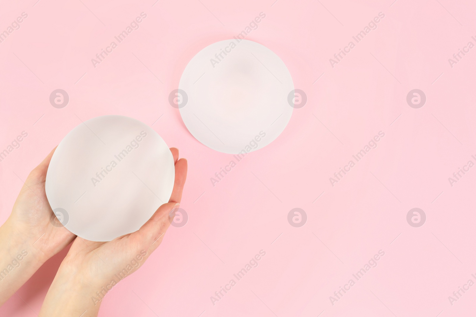 Photo of Woman holding silicone implant for breast augmentation on color background, top view with space for text. Cosmetic surgery