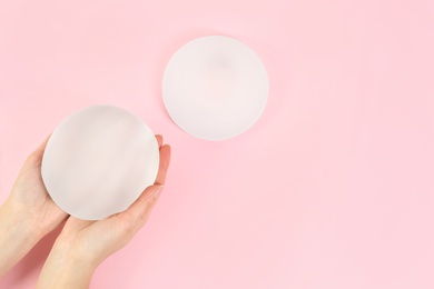 Woman holding silicone implant for breast augmentation on color background, top view with space for text. Cosmetic surgery