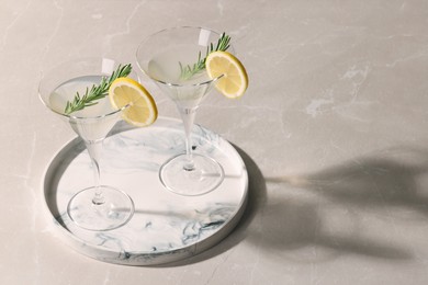 Photo of Tray with martini glasses of fresh cocktail, rosemary and lemon slices on beige marble table. Space for text