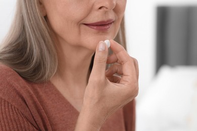 Senior woman taking pill on blurred background, closeup
