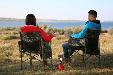 Couple resting in camping chairs and enjoying hot drink outdoors, back view