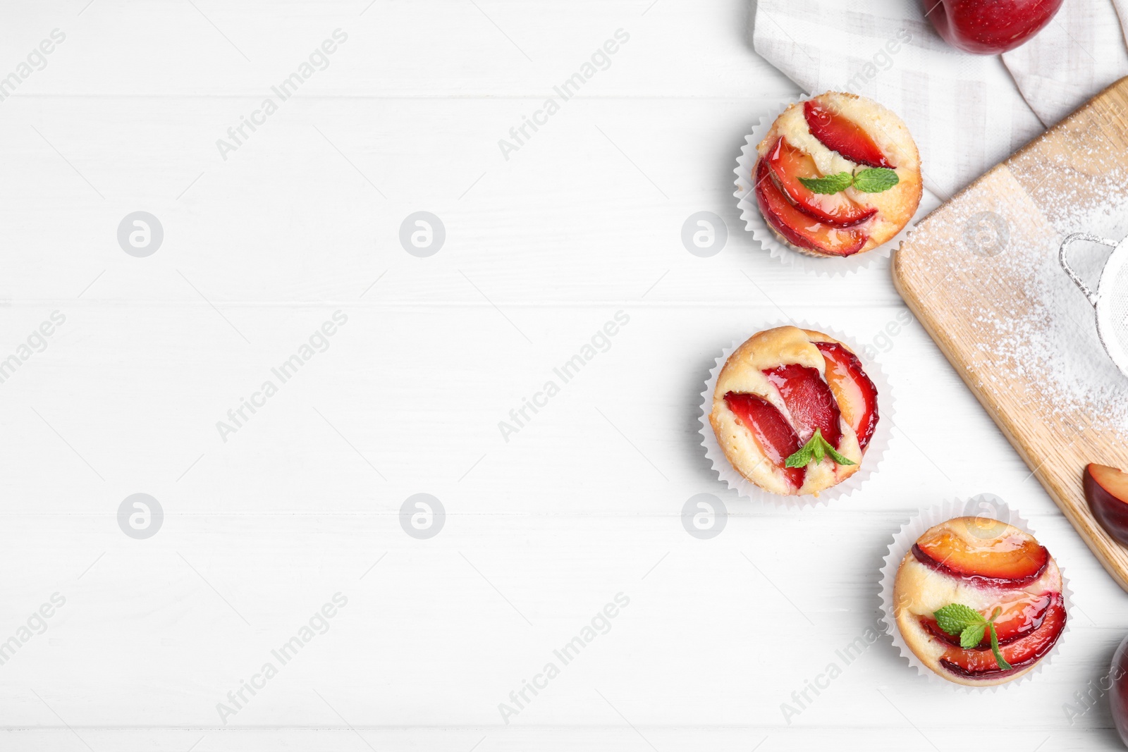 Photo of Delicious cupcakes with plums on white wooden table, flat lay. Space for text