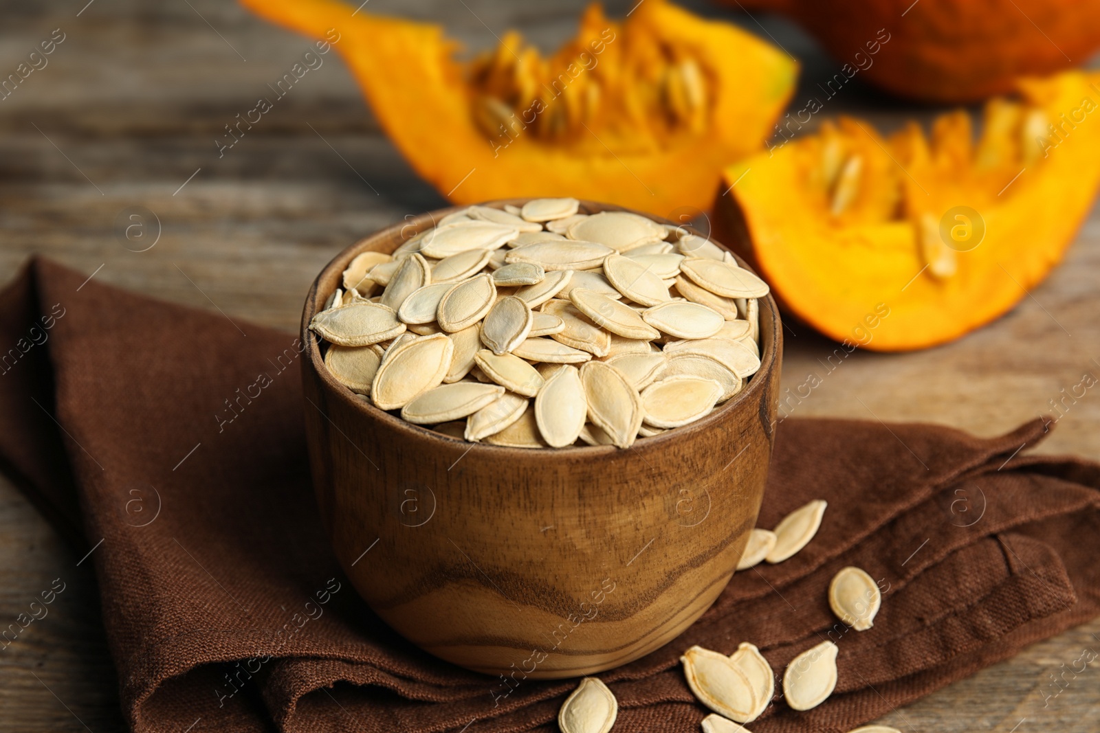 Photo of Bowl of raw unpeeled pumpkin seeds on wooden table