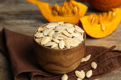 Photo of Bowl of raw unpeeled pumpkin seeds on wooden table