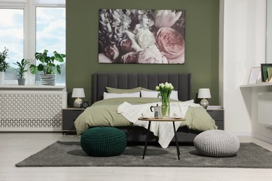 Stylish bedroom with comfortable bed, bedside tables and vase of tulips. Interior design