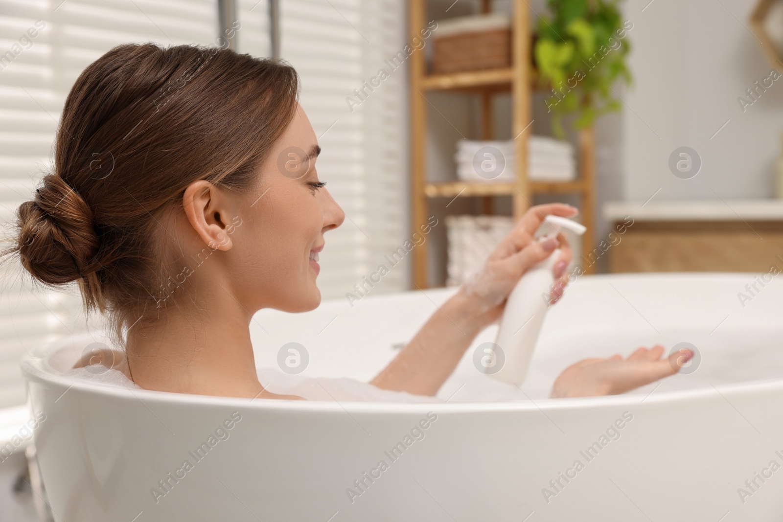 Photo of Woman applying shower gel onto hand in bath indoors