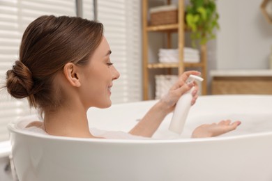 Woman applying shower gel onto hand in bath indoors