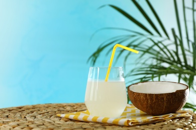 Photo of Composition with glass of coconut water on wicker table against blue background. Space for text