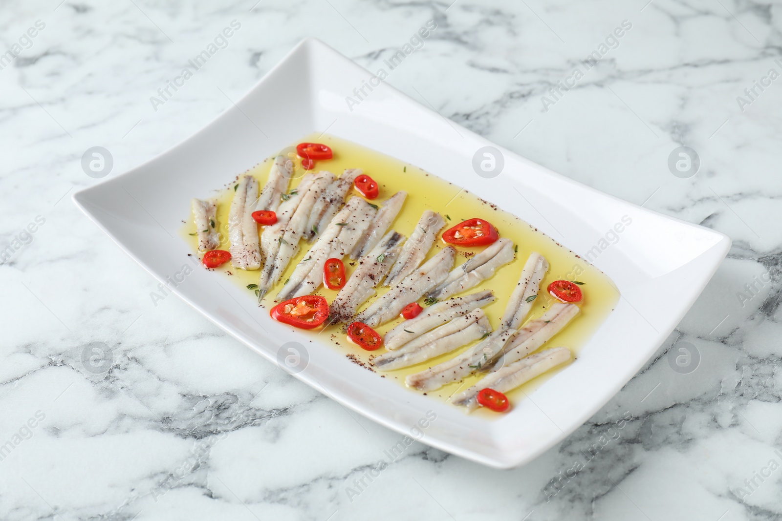 Photo of Tasty pickled anchovies with spices on white marble table