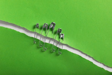 Photo of Pieces of green paper sheets joined with safety pins on white background, top view