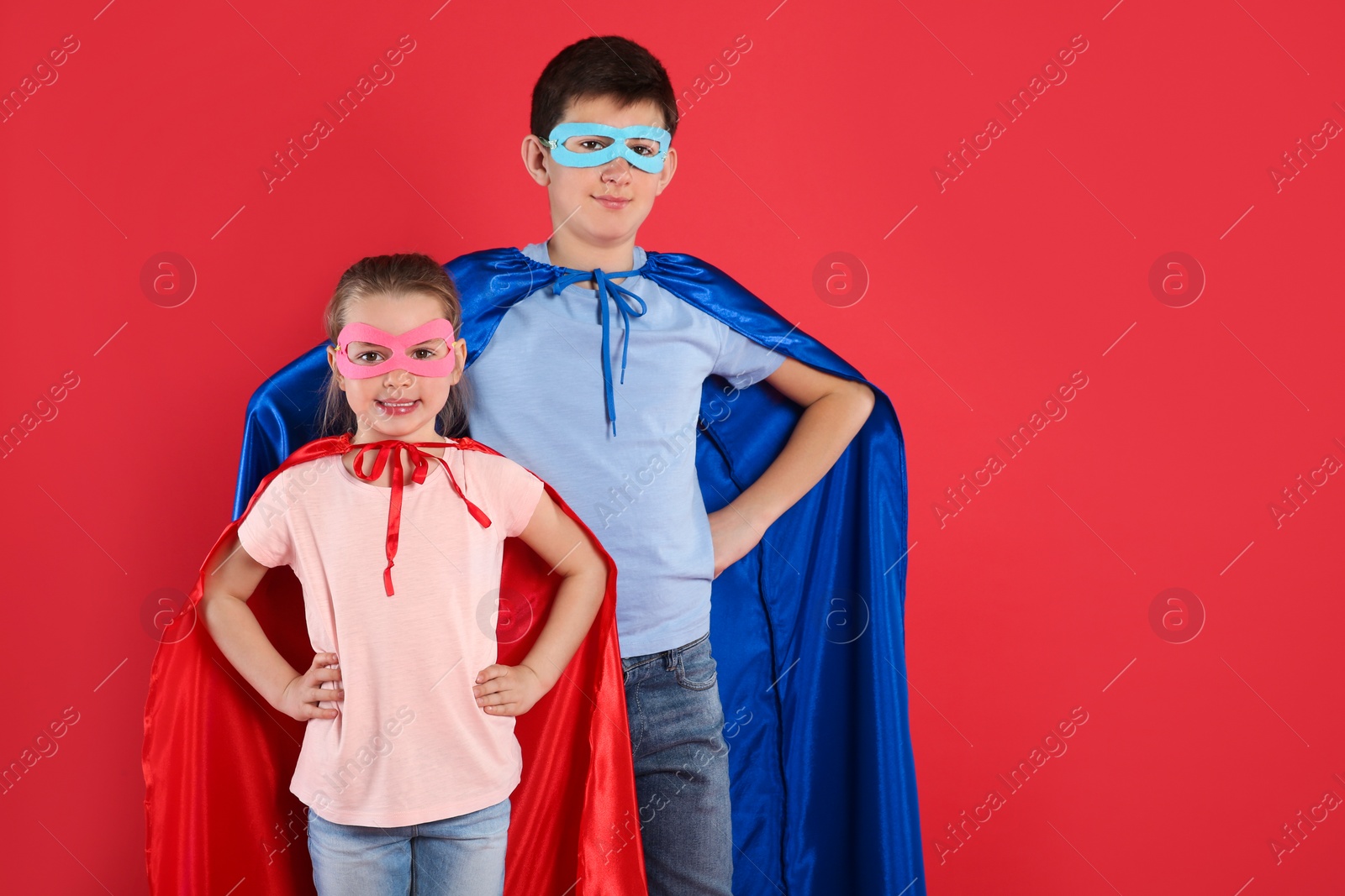 Photo of Boy and little girl in superhero costumes on red background. Space for text