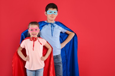 Photo of Boy and little girl in superhero costumes on red background. Space for text