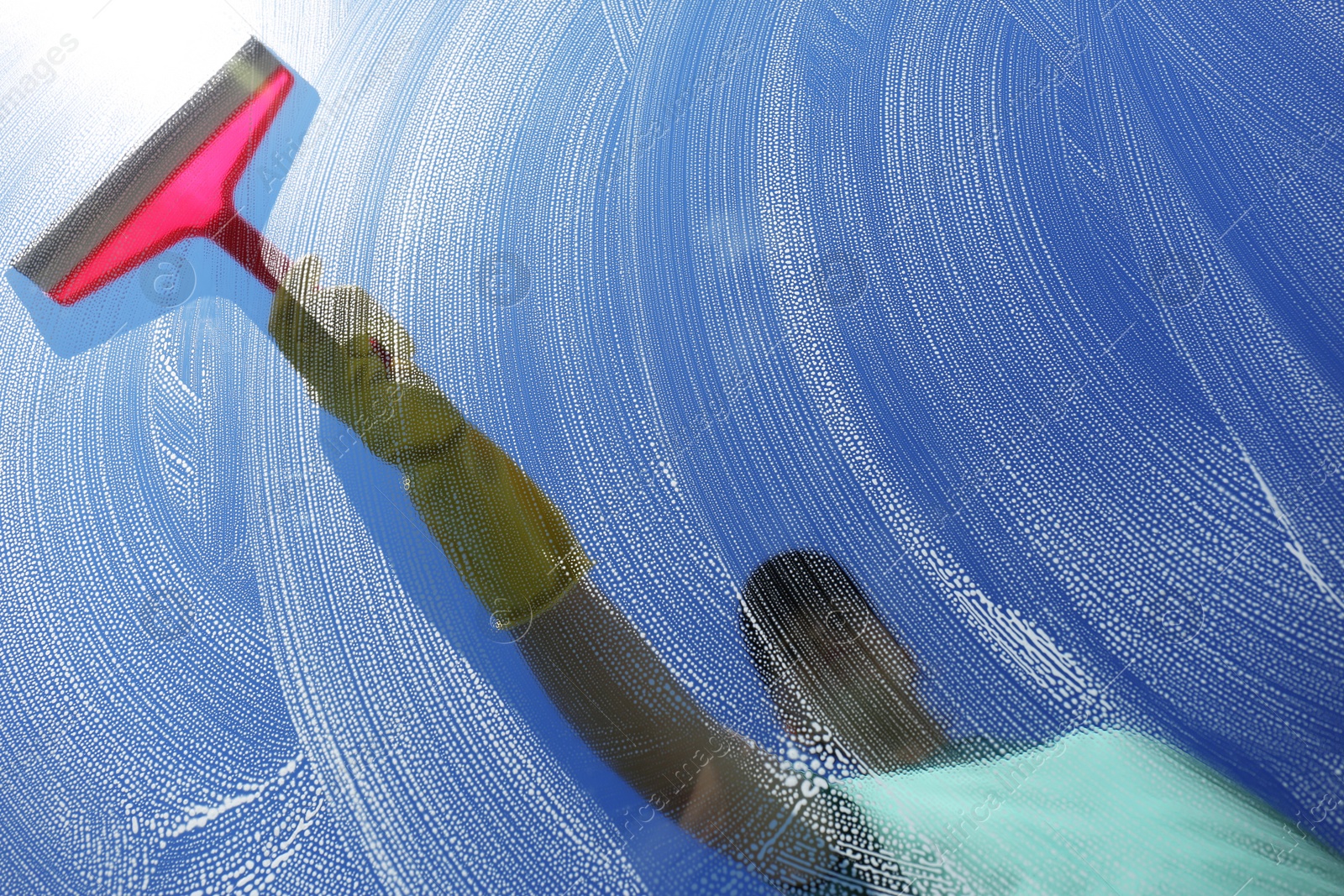 Photo of Woman cleaning glass with squeegee on sunny day