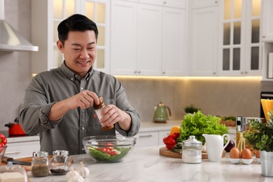 Photo of Cooking process. Man adding salt into bowl of salad at countertop in kitchen