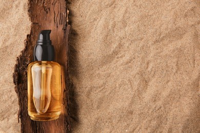 Bottle of serum and tree bark on sand, top view. Space for text
