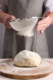 Photo of Man sprinkling flour over dough at table near grey wall, closeup