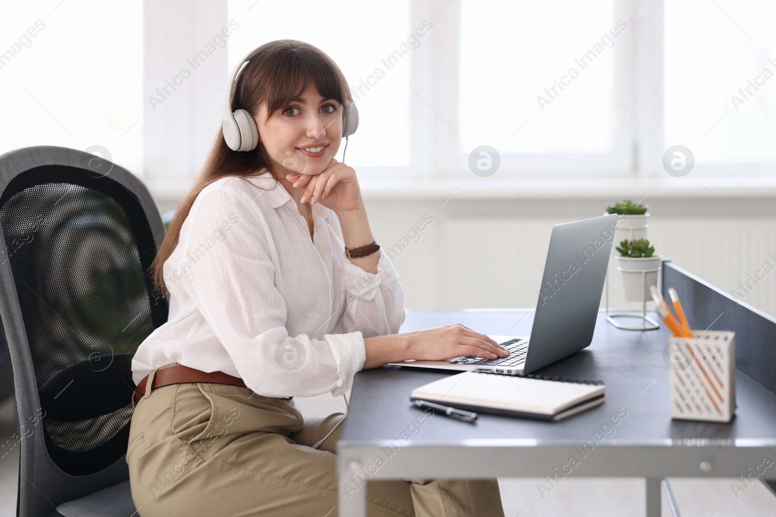 Photo of Woman in headphones watching webinar at table in office