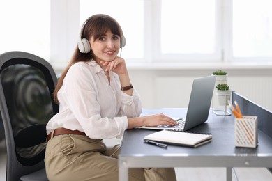 Photo of Woman in headphones watching webinar at table in office