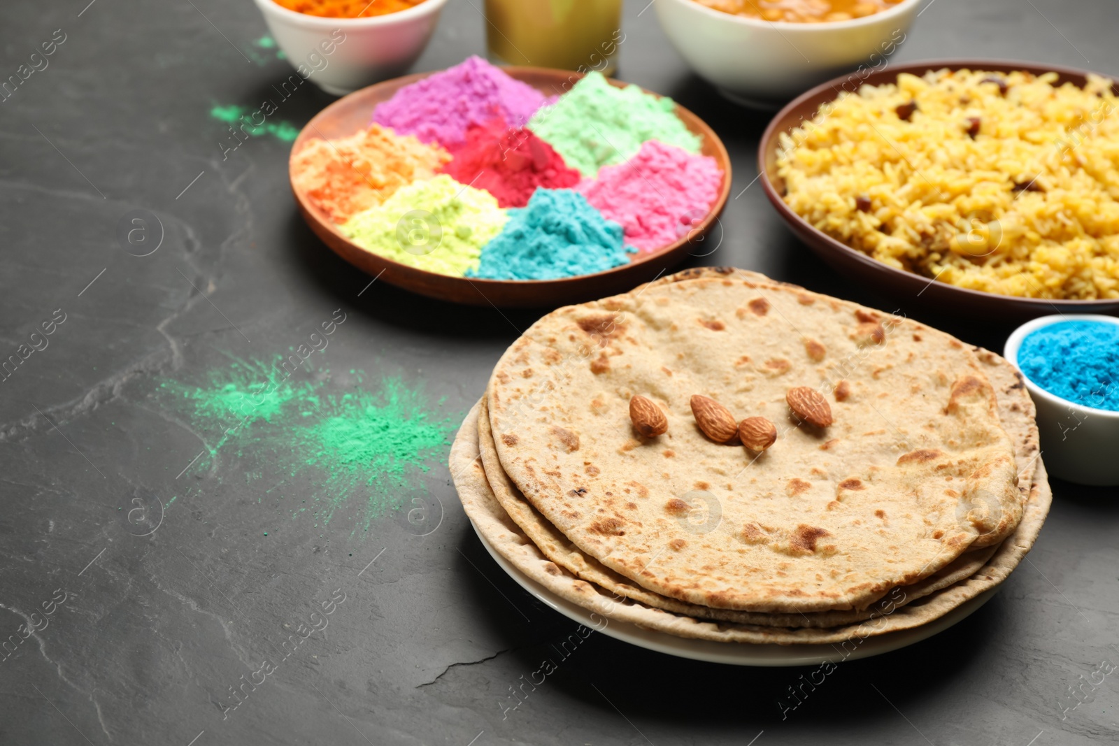 Photo of Traditional Indian food and color powders on black table. Holi festival celebration