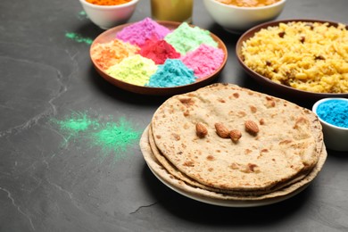 Photo of Traditional Indian food and color powders on black table. Holi festival celebration