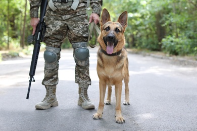 Photo of Man in military uniform with German shepherd dog, outdoors