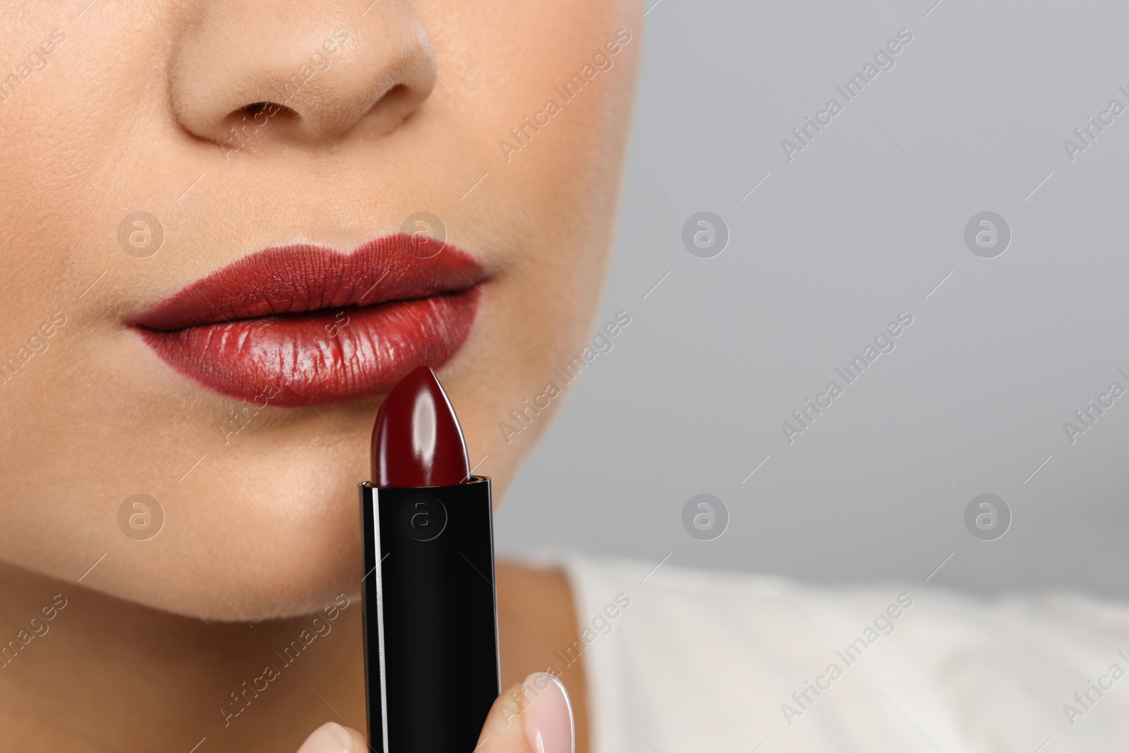 Photo of Beautiful woman applying dark lipstick on gray background, closeup. Space for text