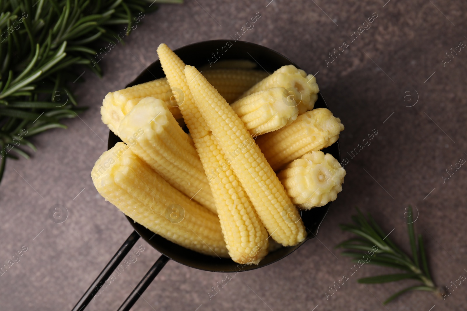 Photo of Tasty fresh yellow baby corns in dish on brown table, top view