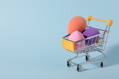 Makeup sponges in small shopping cart on light blue background. Space for text