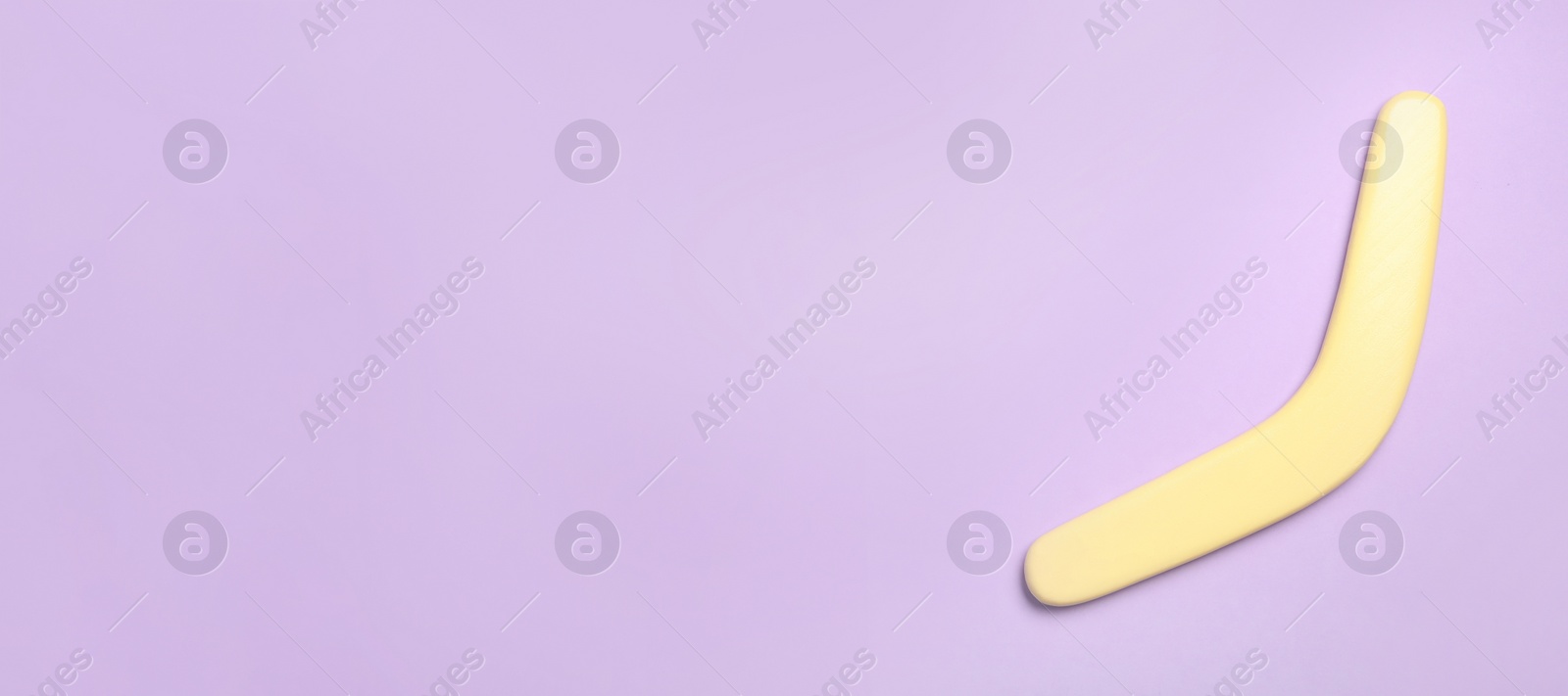 Photo of Yellow wooden boomerang on lilac background, top view. Space for text