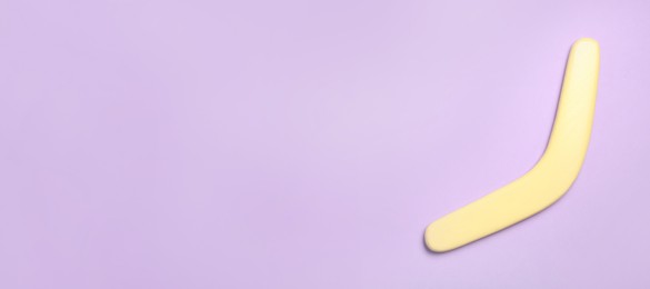 Photo of Yellow wooden boomerang on lilac background, top view. Space for text