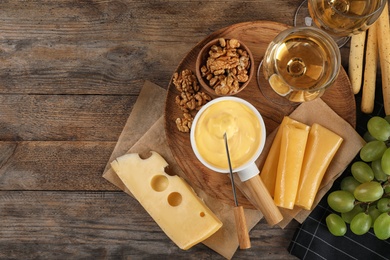 Flat lay composition with pot of tasty cheese fondue and products on wooden table, space for text