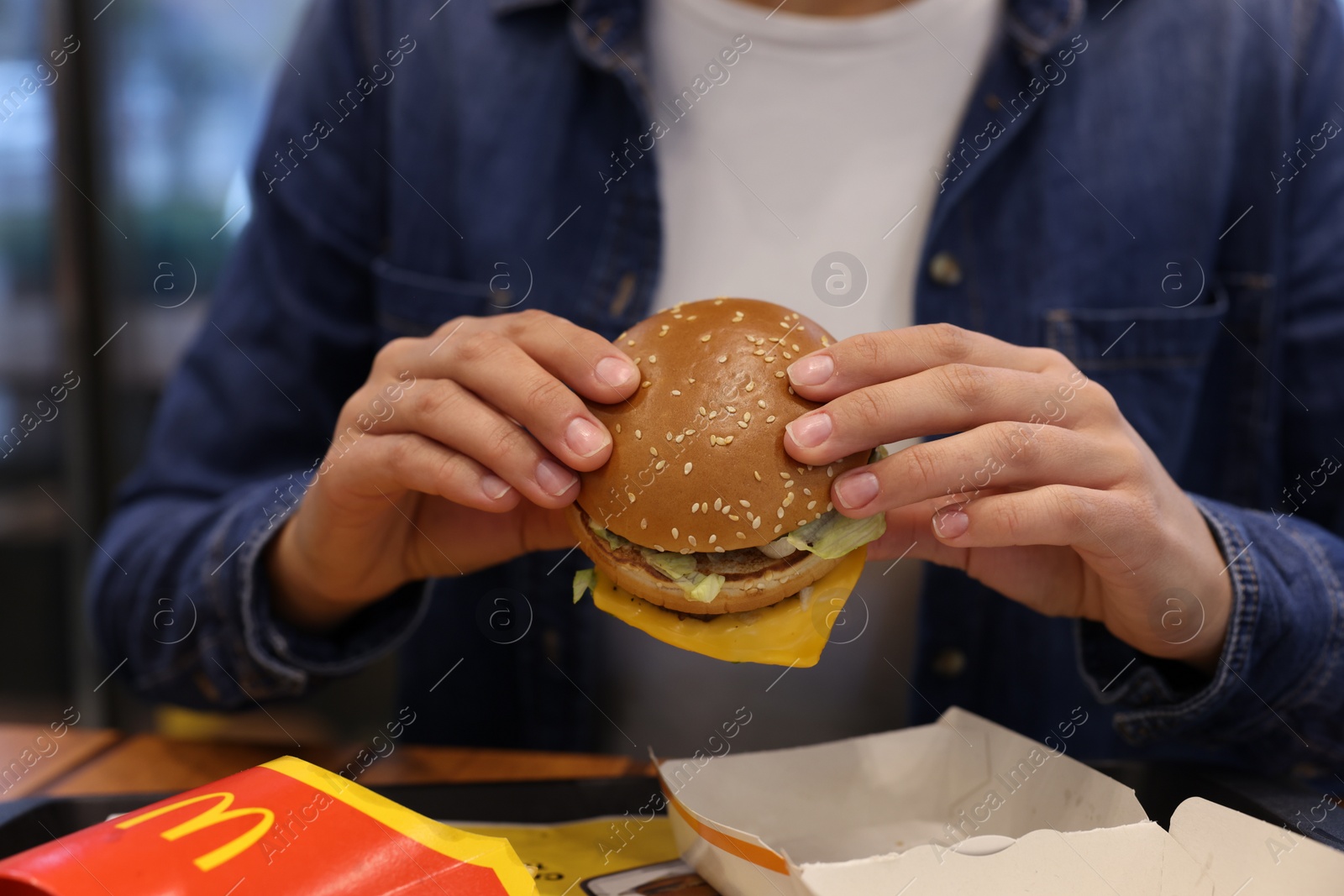 Photo of Lviv, Ukraine - October 9, 2023: Woman with McDonald's burger at table in restaurant, closeup