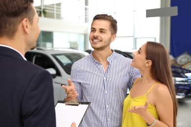 Photo of Young couple choosing new car with salesman in salon