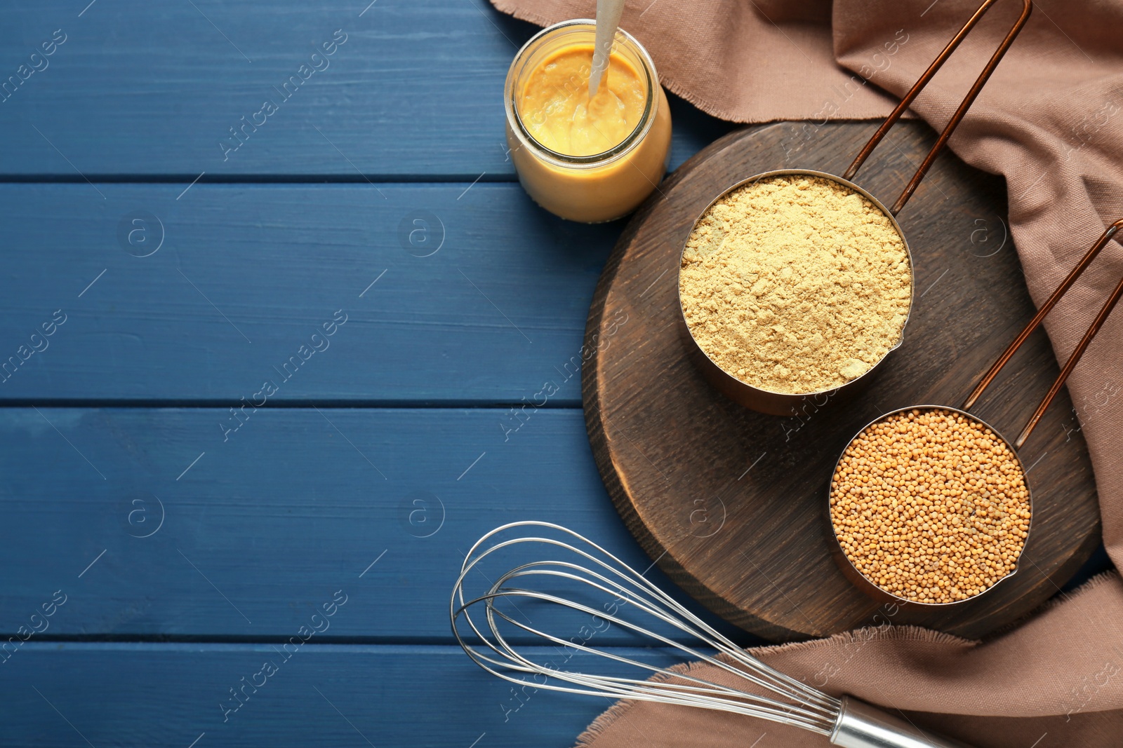 Photo of Saucepans with mustard powder and seeds on blue wooden table, flat lay. Space for text