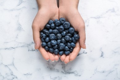 Photo of Woman with heap of tasty blueberries on white marble background, top view