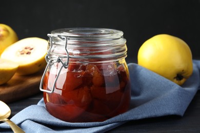 Photo of Quince jam in glass jar, spoon and fresh raw fruits on table, closeup
