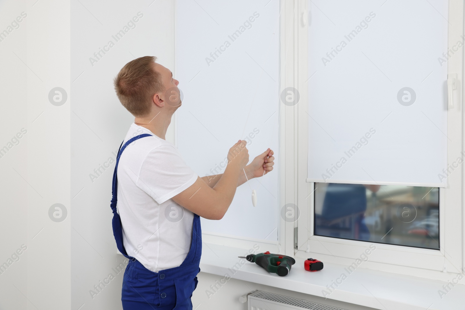 Photo of Worker in uniform opening roller window blind indoors