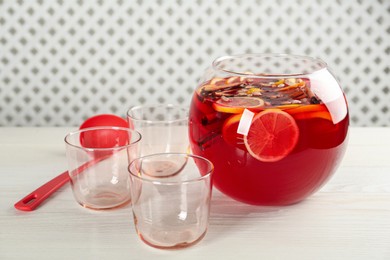 Photo of Bowl of delicious aromatic punch drink, ladle and empty glasses on white wooden table