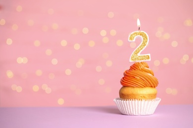 Photo of Birthday cupcake with number two candle on table against festive lights, space for text