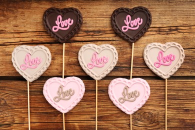 Photo of Different chocolate heart shaped lollipops with word Love on wooden table, flat lay