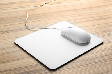 Photo of Modern wired optical mouse and pad on wooden table