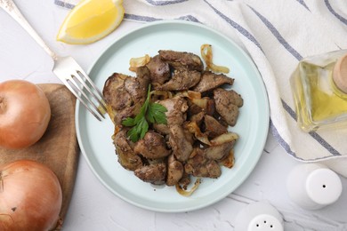 Photo of Tasty fried chicken liver with onion and parsley served on white textured table, flat lay