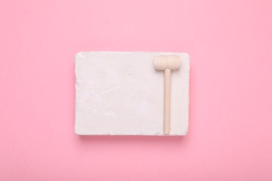 Photo of Educational toy for motor skills development. Excavation kit (plaster and wooden mallet) on pink background, top view