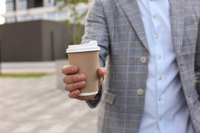 Coffee to go. Man with paper cup of drink outdoors, selective focus. Space for text