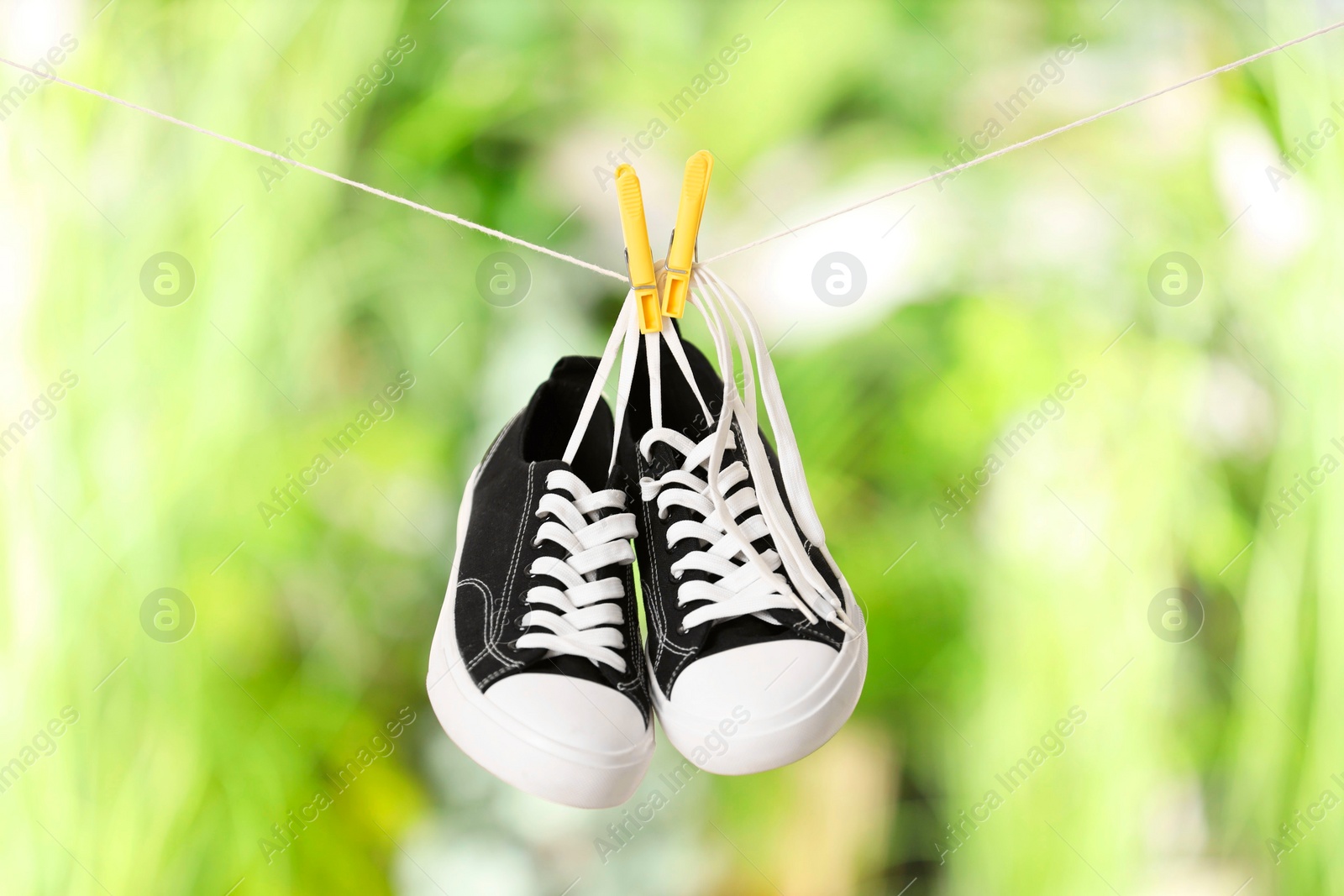 Photo of Stylish sneakers drying on washing line against blurred background