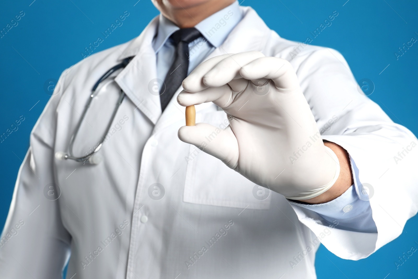 Photo of Doctor holding suppository for hemorrhoid treatment on blue background, closeup