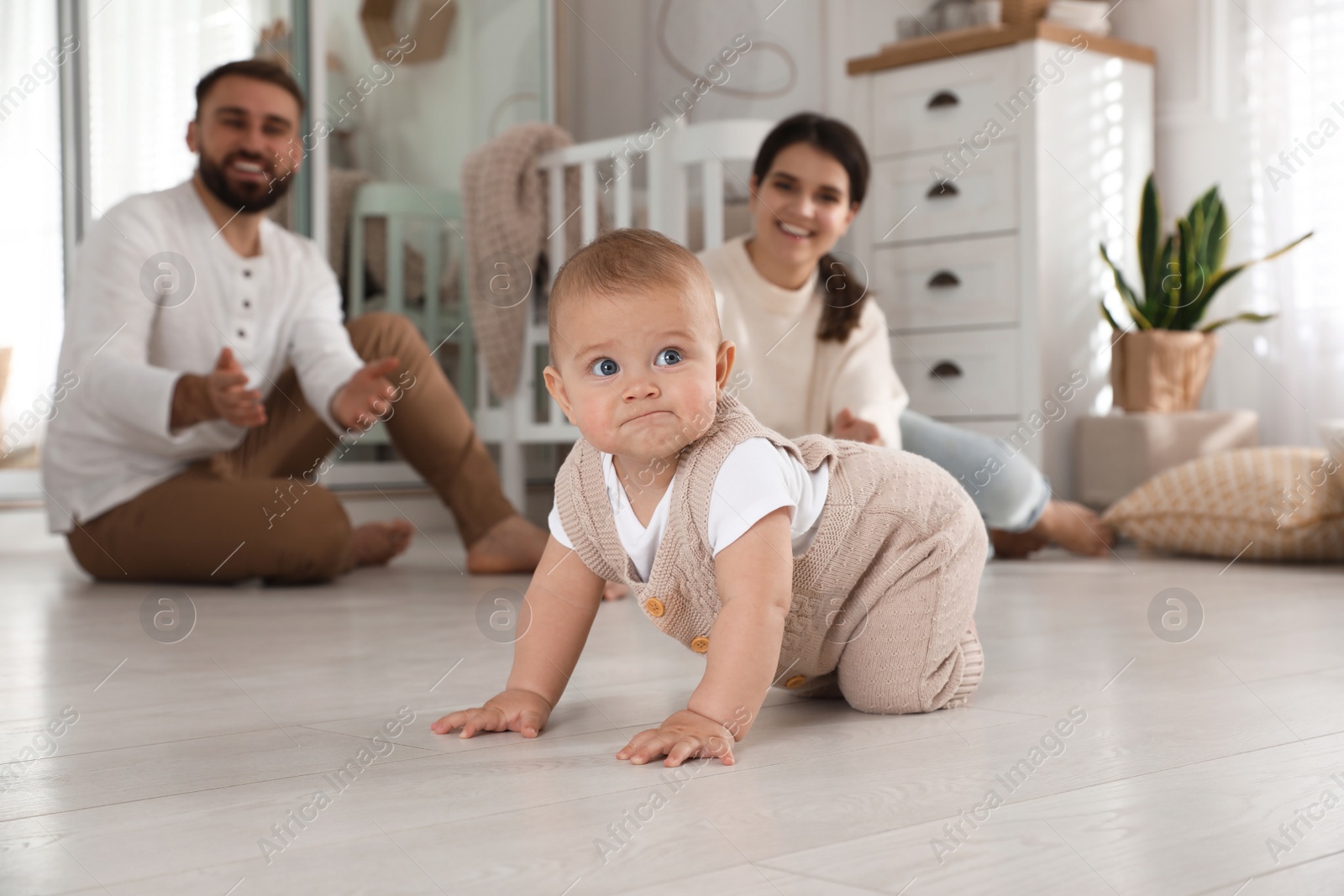 Photo of Happy parents watching their baby crawl on floor at home