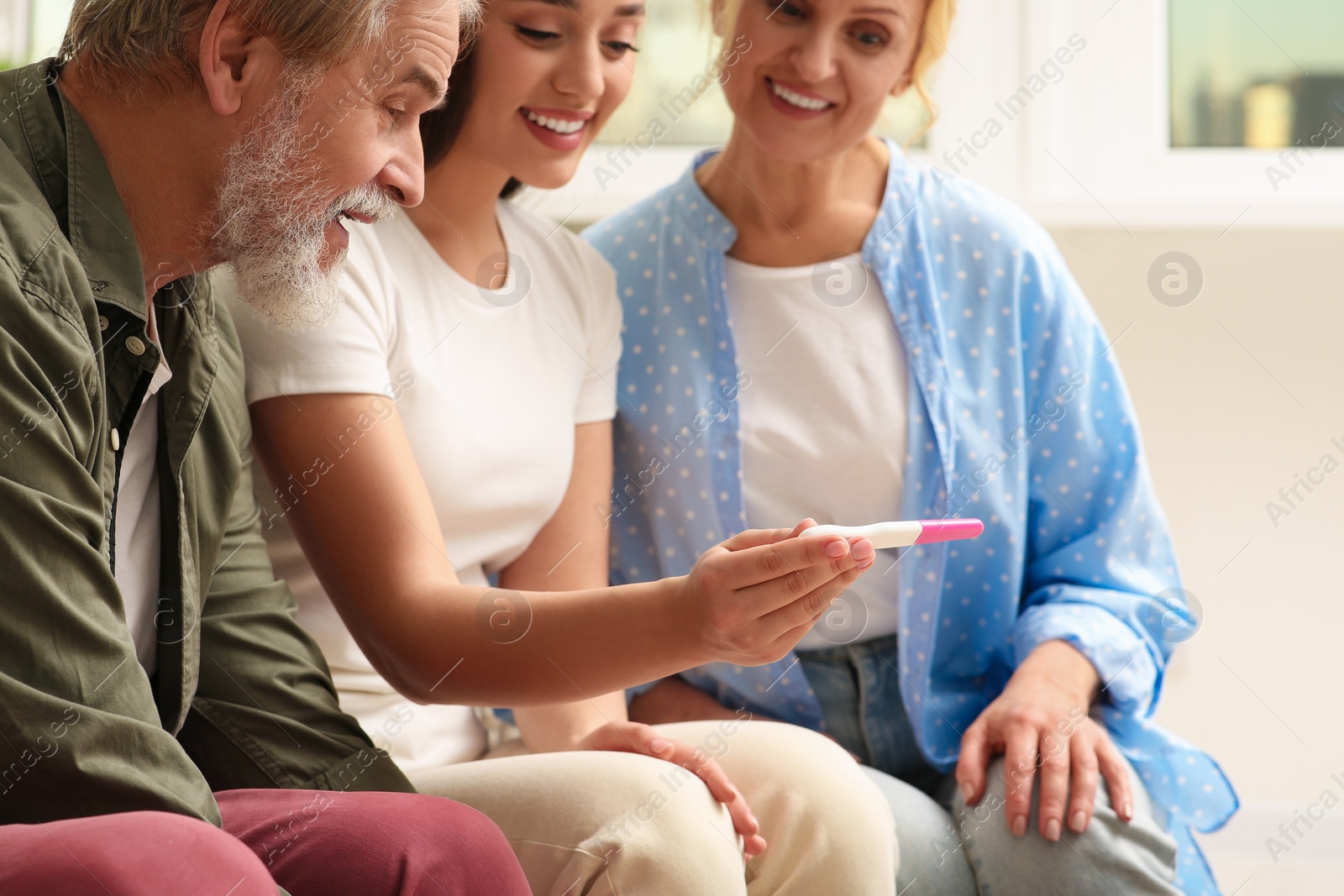 Photo of Happy woman showing her parents pregnancy test at home. Grandparents' reaction to future grandson