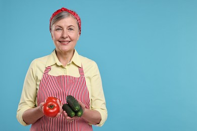 Happy housewife with tomatoes and cucumbers on light blue background, space for text