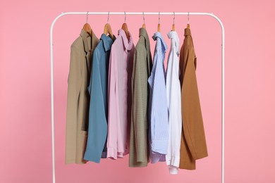 Rack with stylish clothes on wooden hangers against pink background